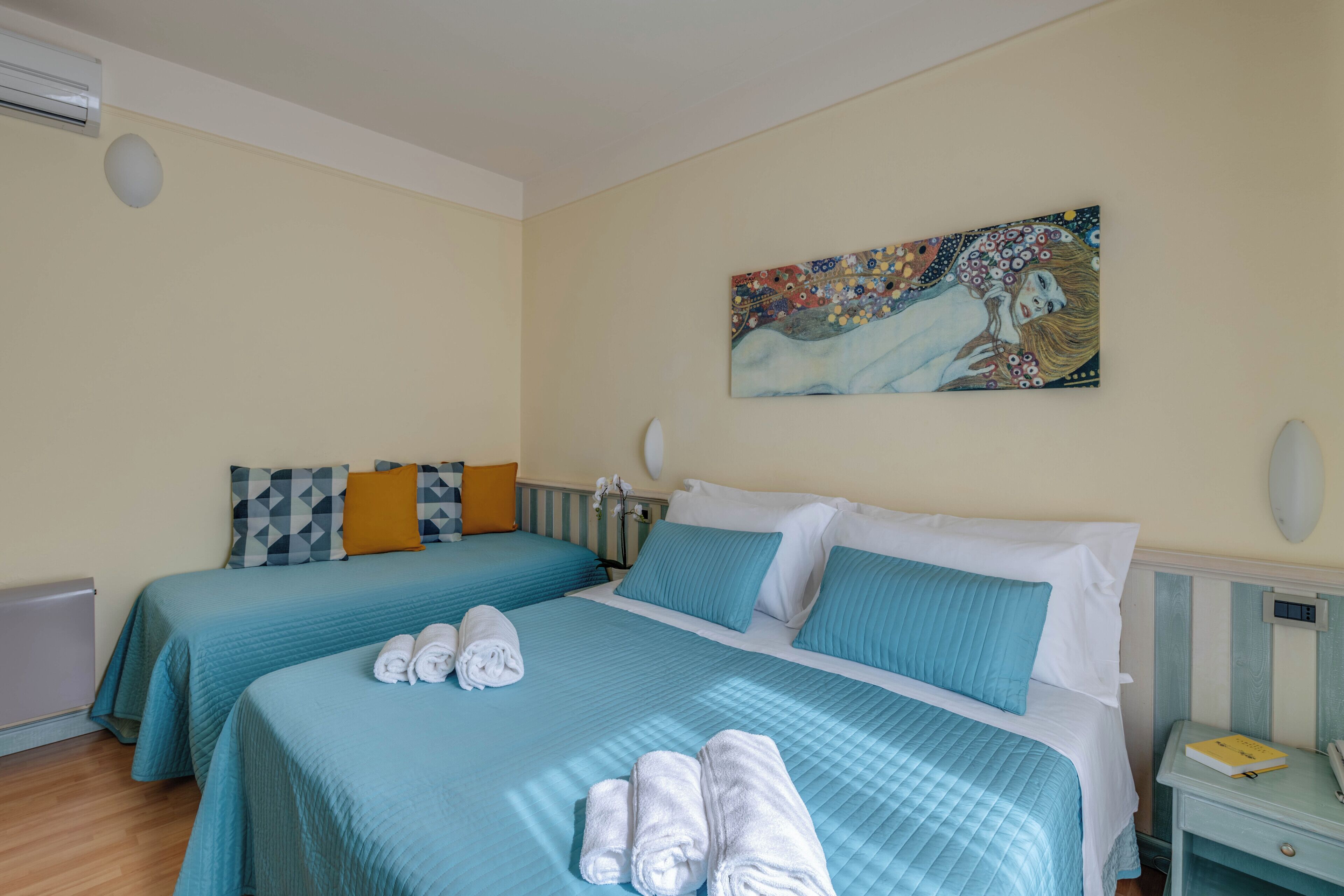 Une chambre d’hôtel avec deux lits, chacun agrémenté de draps bleus et d’oreillers blancs, et un tableau accroché au mur.