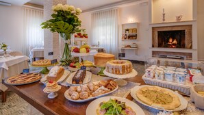 A buffet table with various food items, a vase of flowers, and a fireplace in the background. - Hotel Massimo (Cecina)