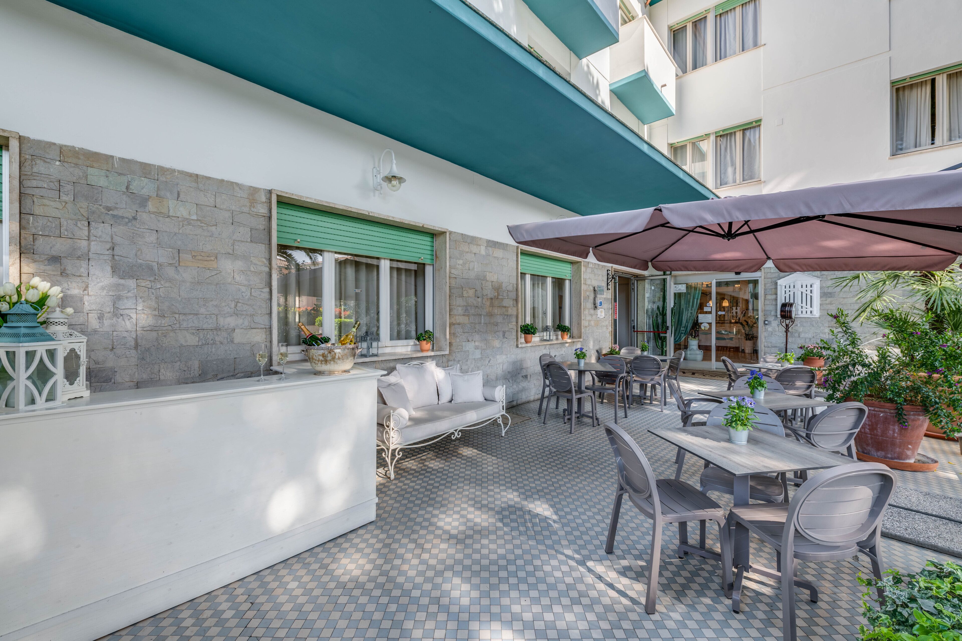 An outdoor patio with a stone wall, a white sofa, and a dining area with tables and chairs.