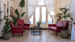 A living room with two red armchairs, a coffee table, and large potted plants. - Hotel Massimo (Cecina)