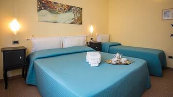 A hotel room with two beds, each with a blue bedspread and white pillows. There is a painting on the wall above the beds, a nightstand with a phone and a tray with a teapot and cups on the bed.