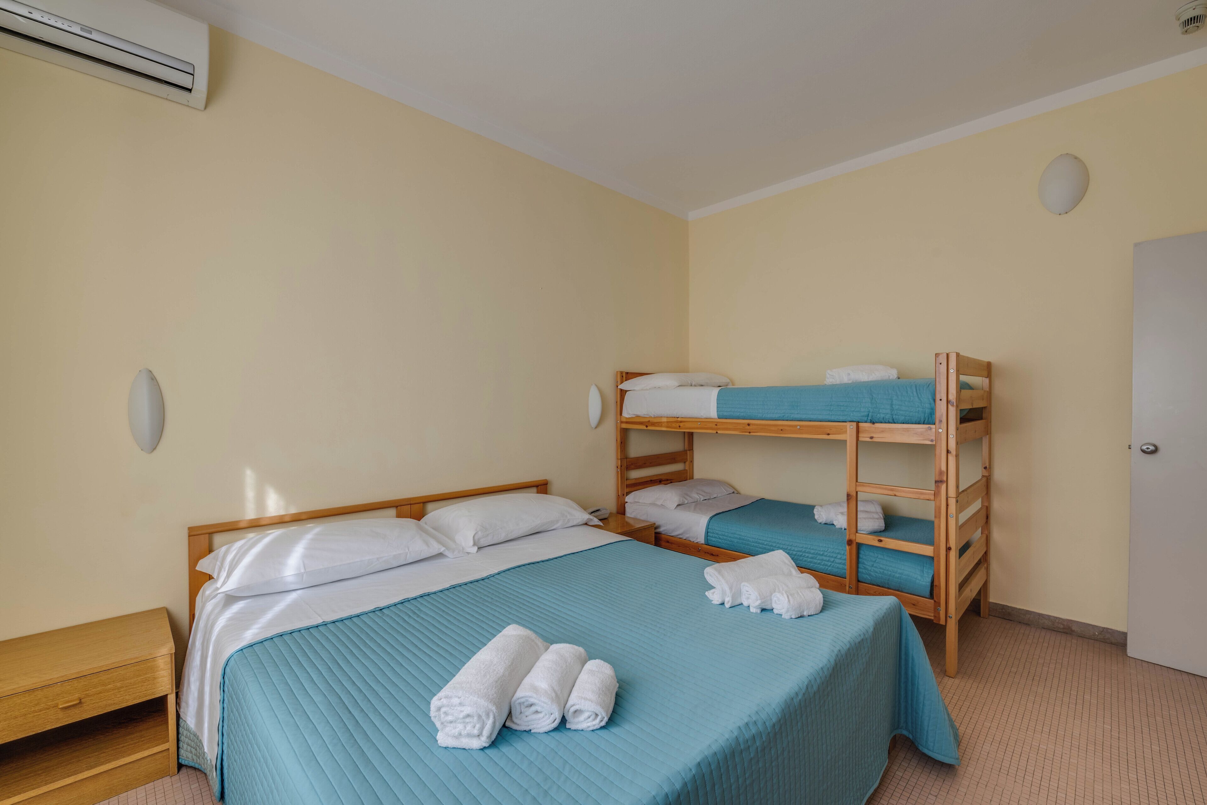 Ein Zimmer mit einem Einzelbett, einem Etagenbett und einem hölzernen Nachttisch.