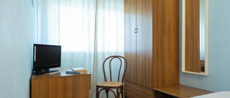 A bedroom with a wooden wardrobe, a desk with a television, a chair, and a bed.