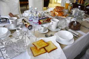 Een ontbijttafel met brood, gebak, waterflesjes en koffiekopjes.