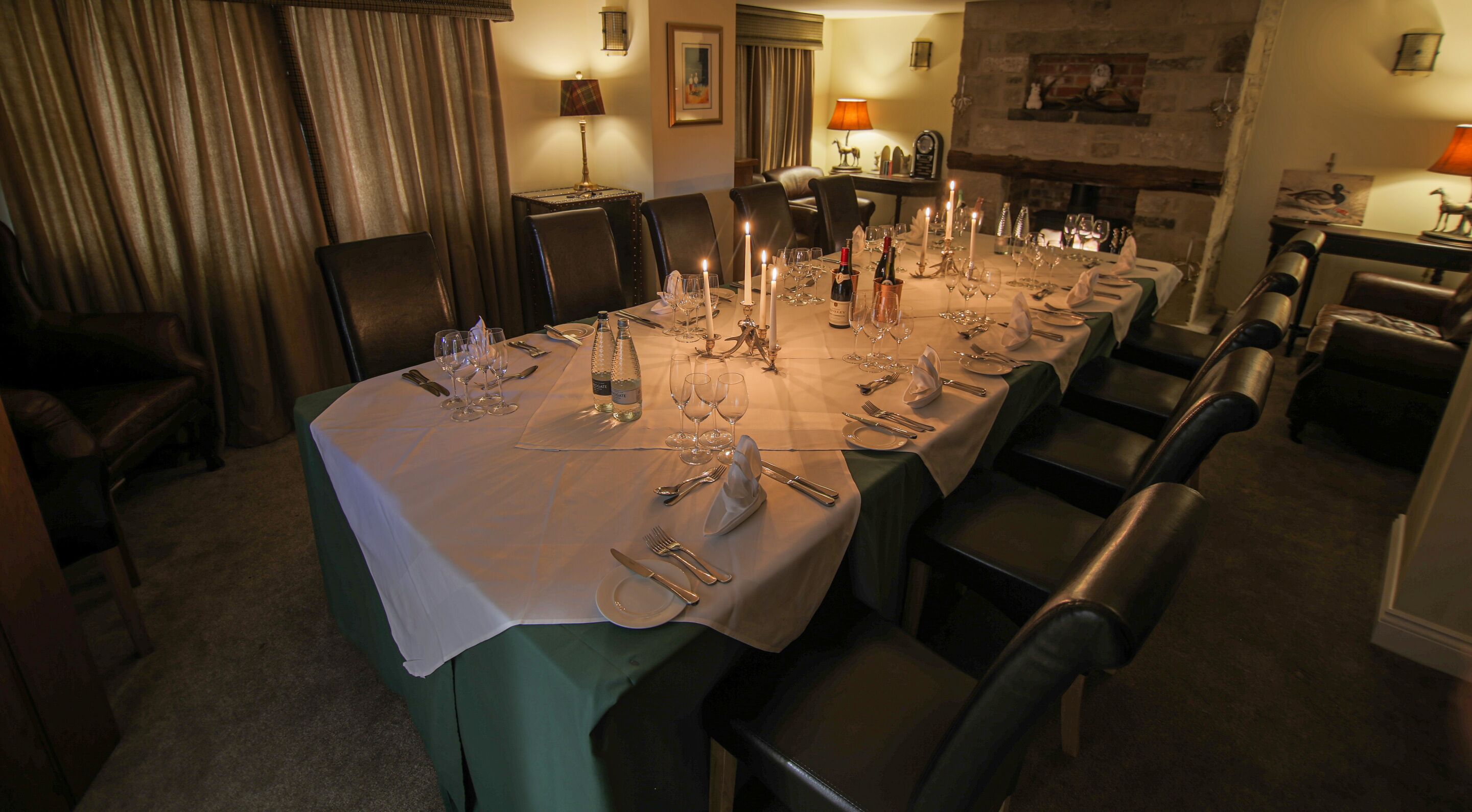 Una larga mesa de comedor dispuesta para una comida, con múltiples sillas, velas y copas de vino.