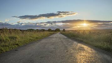 Un camino rural con muros de piedra a un lado y hierba al otro, que se dirige hacia un atardecer.