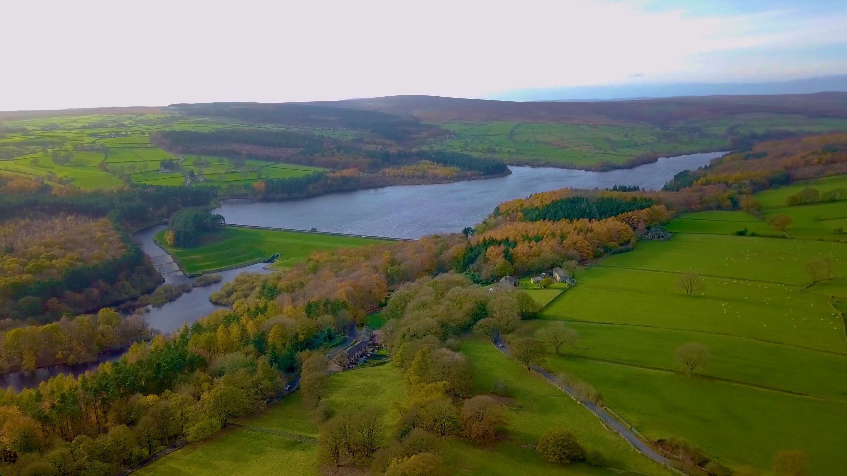 An aerial view of a river meandering through a valley with fields and trees, surrounded by rolling hills.
