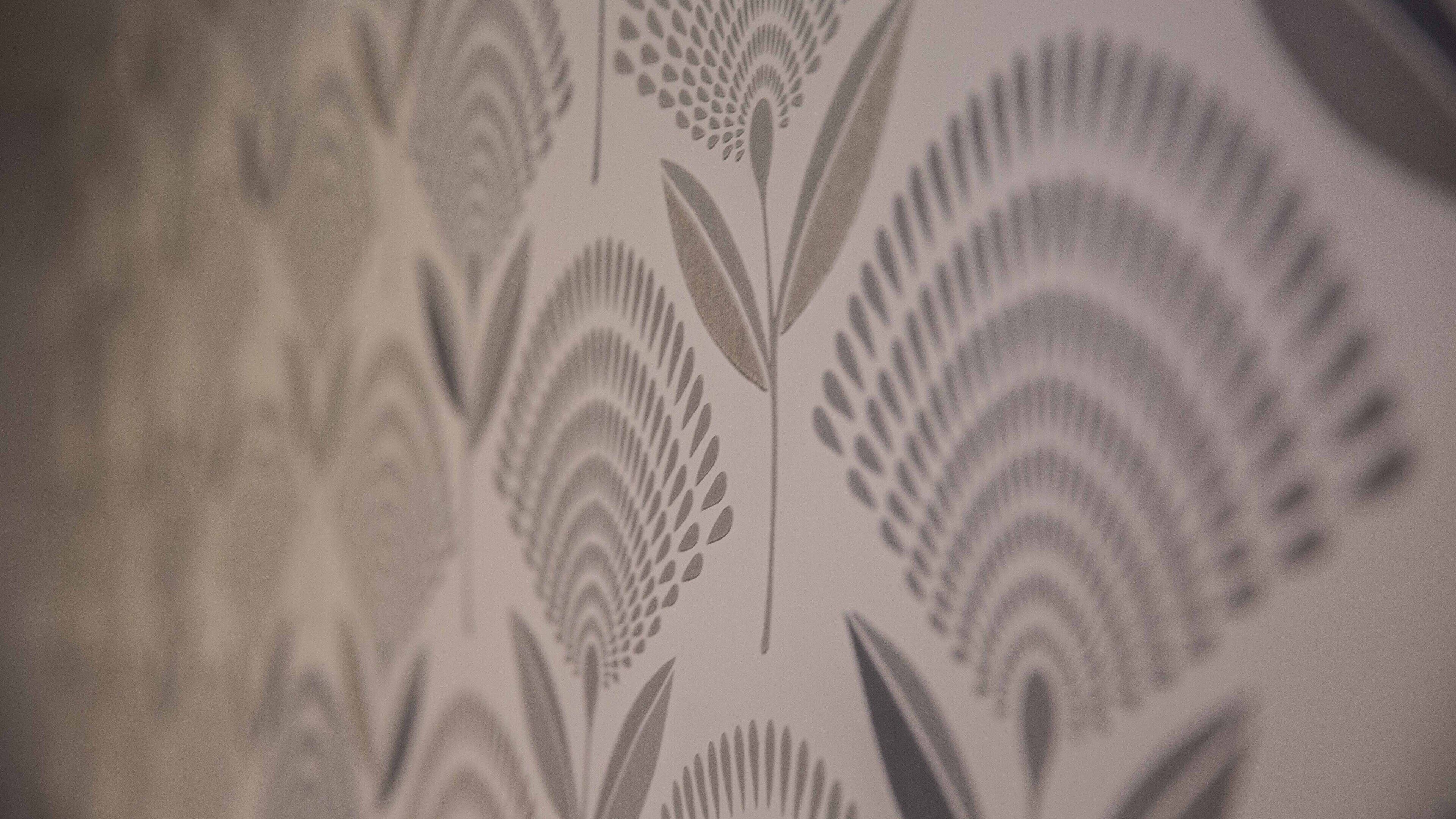 Un gros plan d’un papier peint orné d’un motif répétitif de feuilles et de fleurs stylisées.