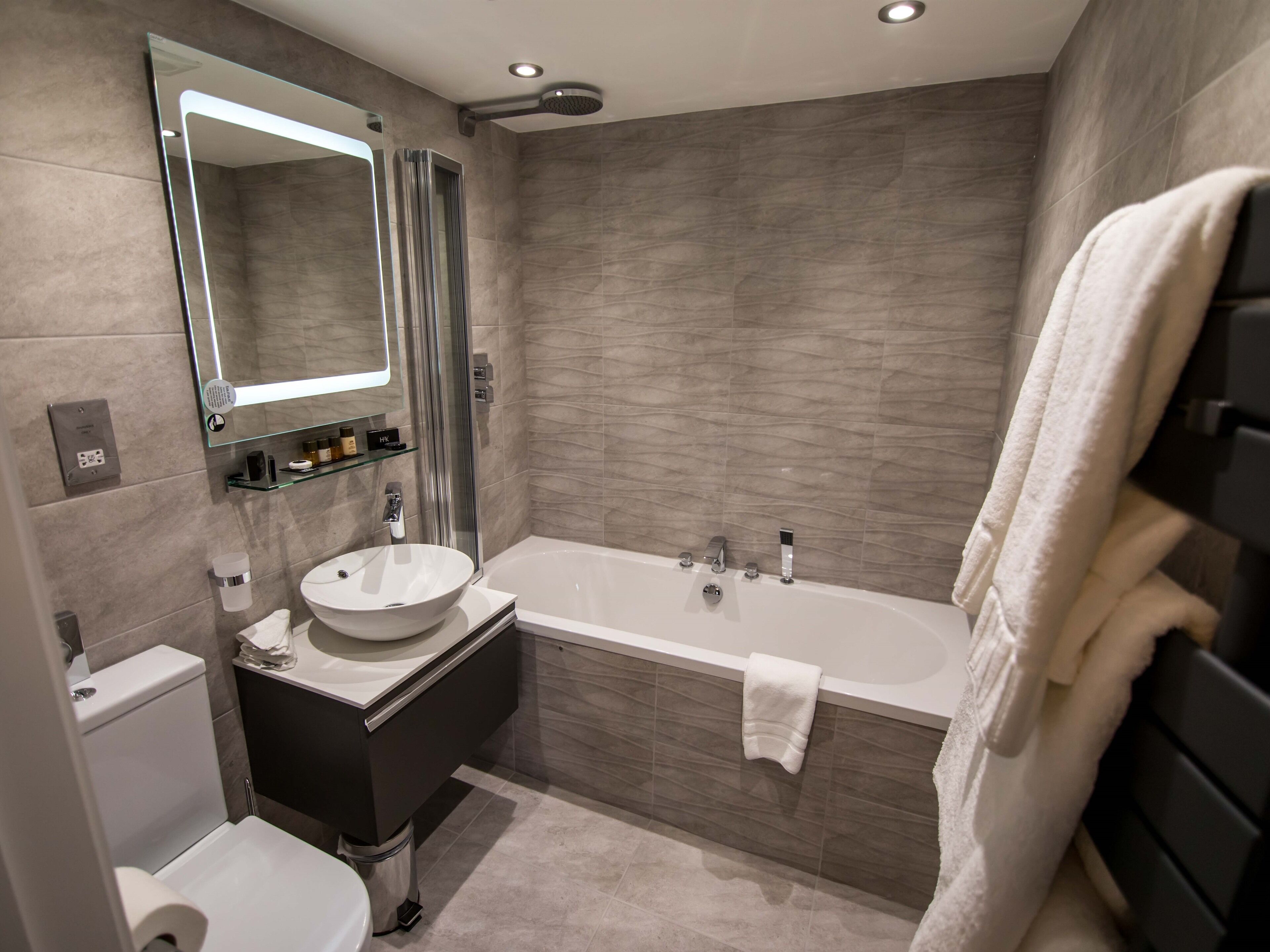 A modern bathroom with a large bathtub, a round sink, a toilet, and a glass shower enclosure.
