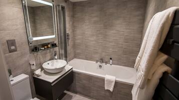 A modern bathroom with a large bathtub, a round sink, a toilet, and a glass shower enclosure.