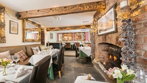 Un restaurante acogedor con chimenea de ladrillo, vigas de madera y mesas dispuestas para comer.