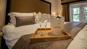 Una habitación de hotel con una cama, una bandeja de madera con una botella de champán y una bandeja con dos copas de vino.