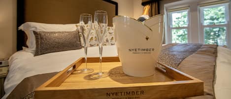 A wooden tray with a Nyetimber champagne bottle and glasses on a bed with a view of trees through the window.