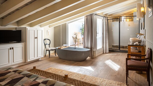 A spacious living room with a large bathtub, wooden beams on the ceiling, a television, and a view of the outdoors. - Hotel Boutique Can Sastre (Ciutadella de Menorca)