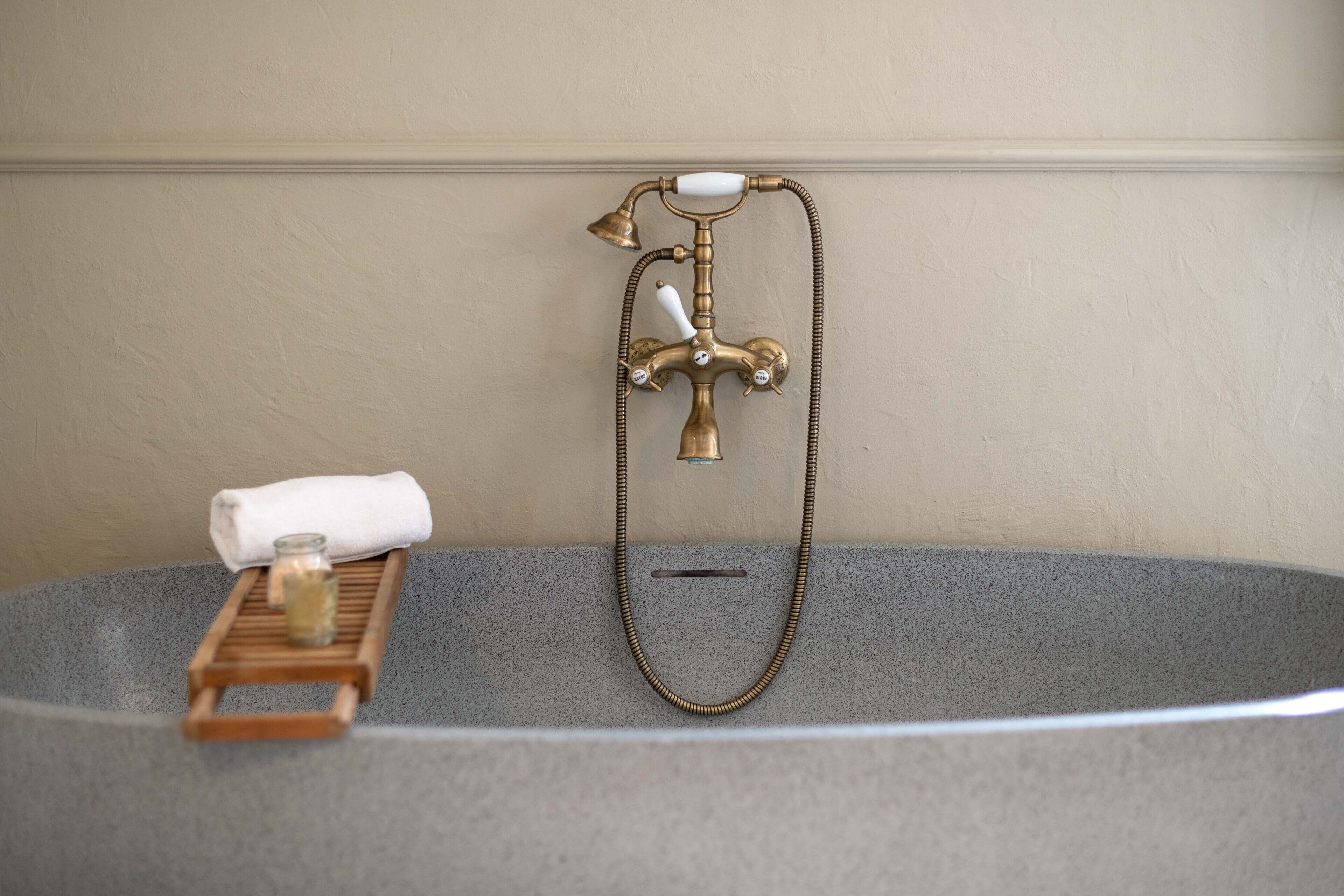 Una bañera con grifo de latón y una bandeja de madera.