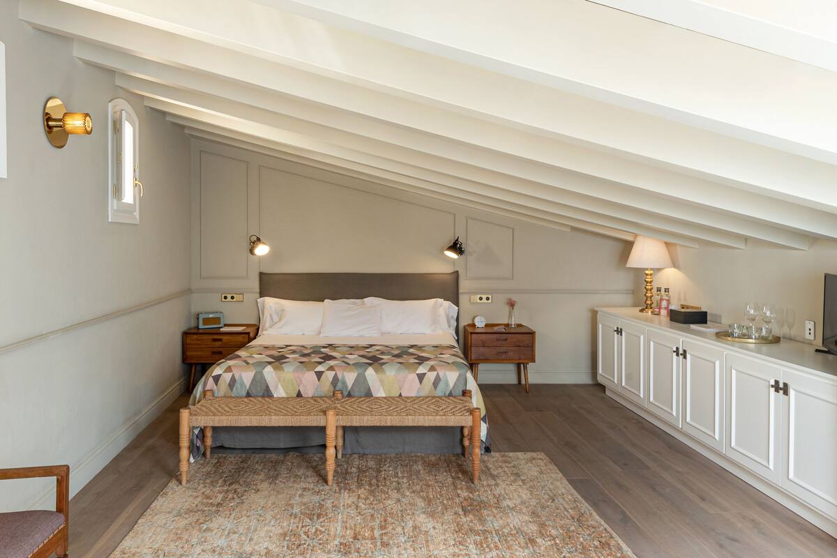 Une chambre à coucher comprenant un lit, des tables de chevet, une commode, un banc, une armoire et un miroir.