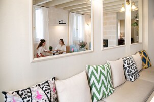 Una sala de estar con un sofá, un comedor con una mesa y sillas, y un espejo grande que refleja la habitación.
