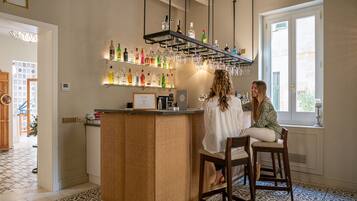 Zona de bar con mostrador de mimbre, estantes con botellas y copas colgantes.