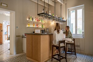 Zona de bar con mostrador de mimbre, estantes con botellas y copas colgantes.