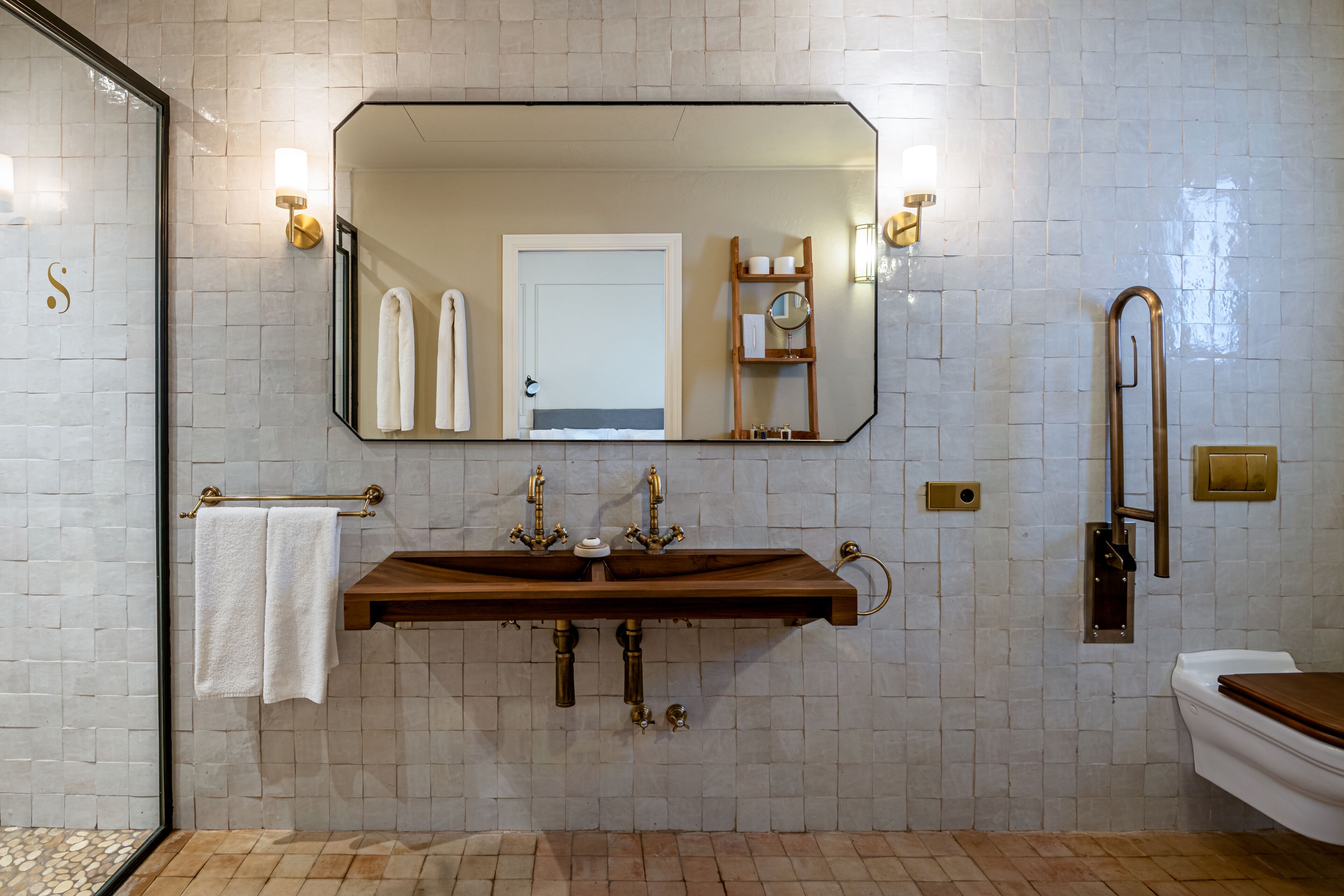 A bathroom with a large mirror, two sinks, a towel rack, and a toilet.