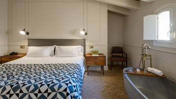 Un dormitorio con cama, mesitas de noche, un sillón, tocador con espejo y una ventana.