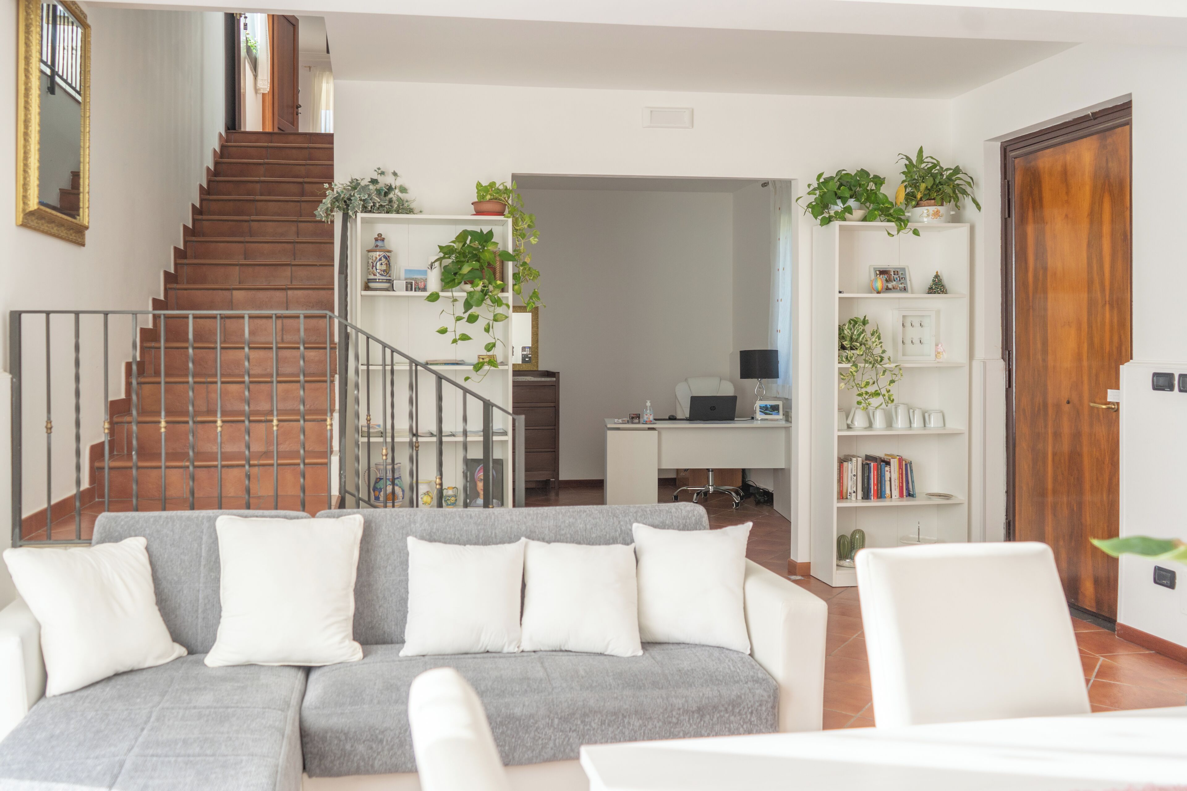 Ein Wohnzimmer mit grauem Sofa, einer Treppe und einem Schreibtisch mit einem Computer.