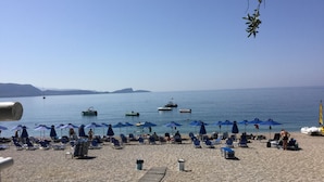 A beach with sun loungers and umbrellas, a wooden walkway, and boats in the water. - Villa Apollo Parga (Parga)