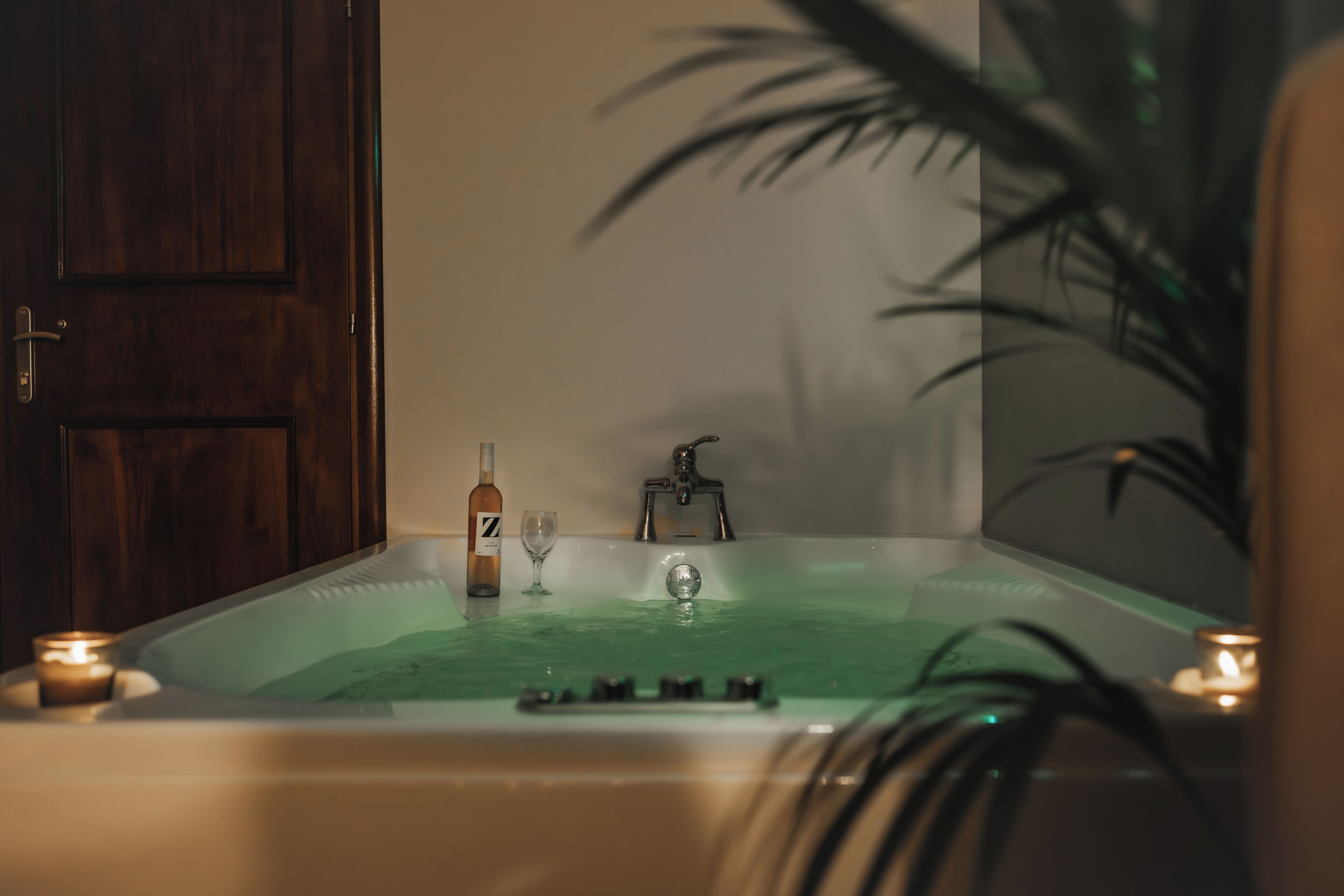 Eine Badewanne mit einer Flasche, einem Glas, einem Wasserhahn und Kerzen.