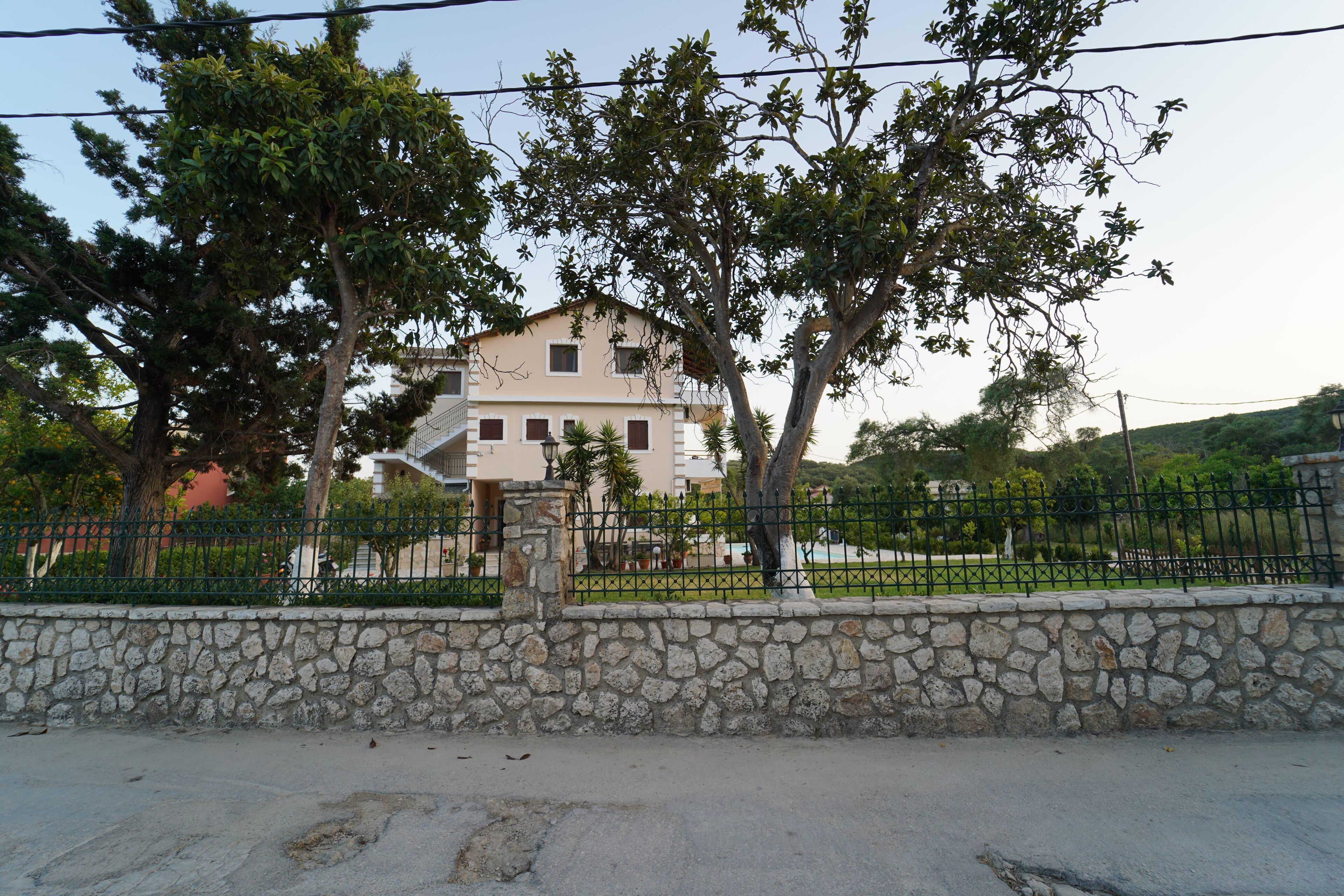 A two-story house with a stone wall in the foreground and a metal fence.