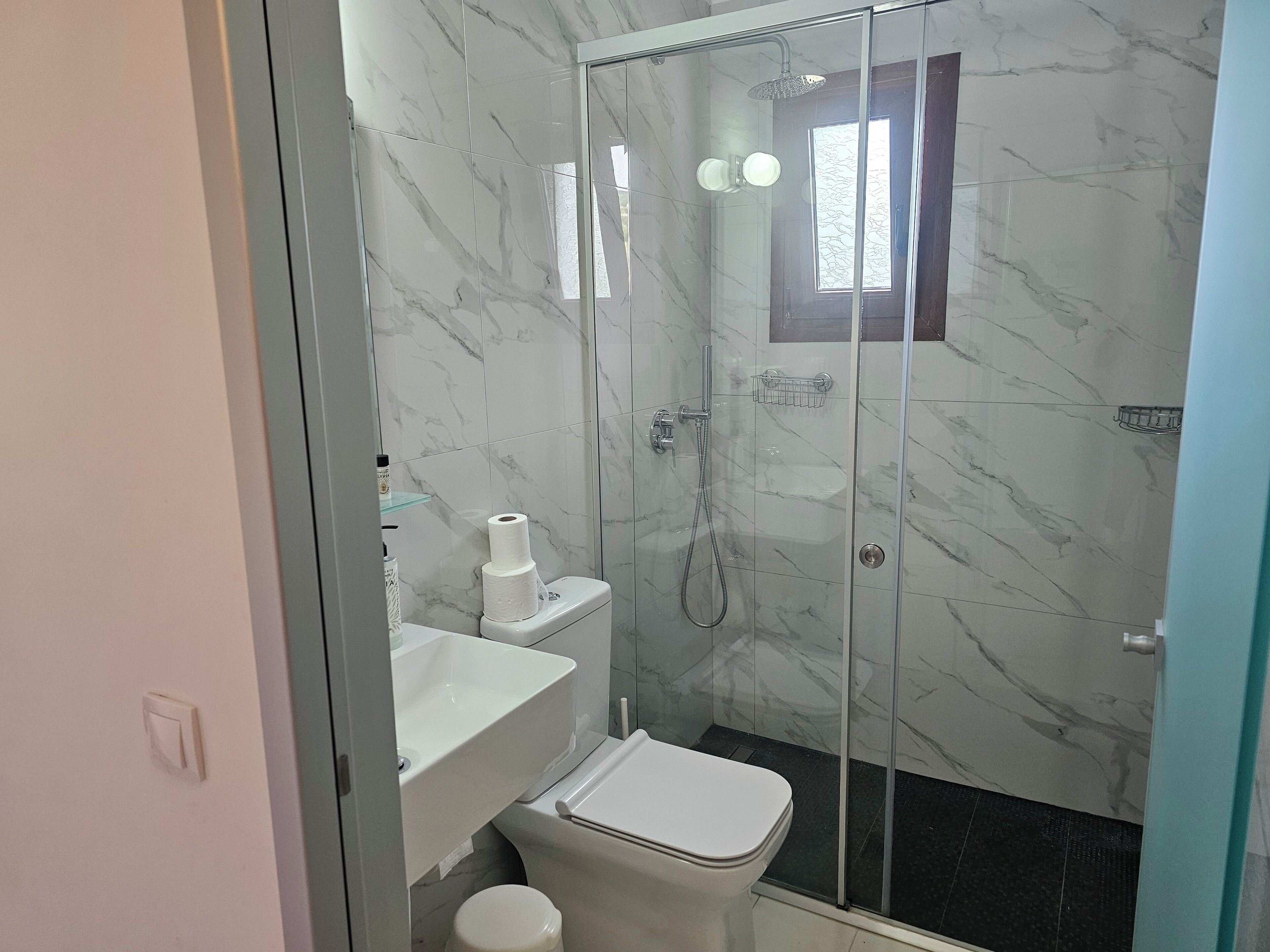 A bathroom with a glass-enclosed shower, a white toilet, and a marble-tiled wall.