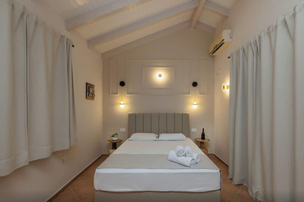 Quarto de hotel com cama, duas mesas de cabeceira, ar condicionado fixado na parede e luminária no teto.