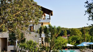 A two-story building with a balcony, a swimming pool with lounge chairs, and a fenced garden area. - Villa Apollo Parga (Parga)