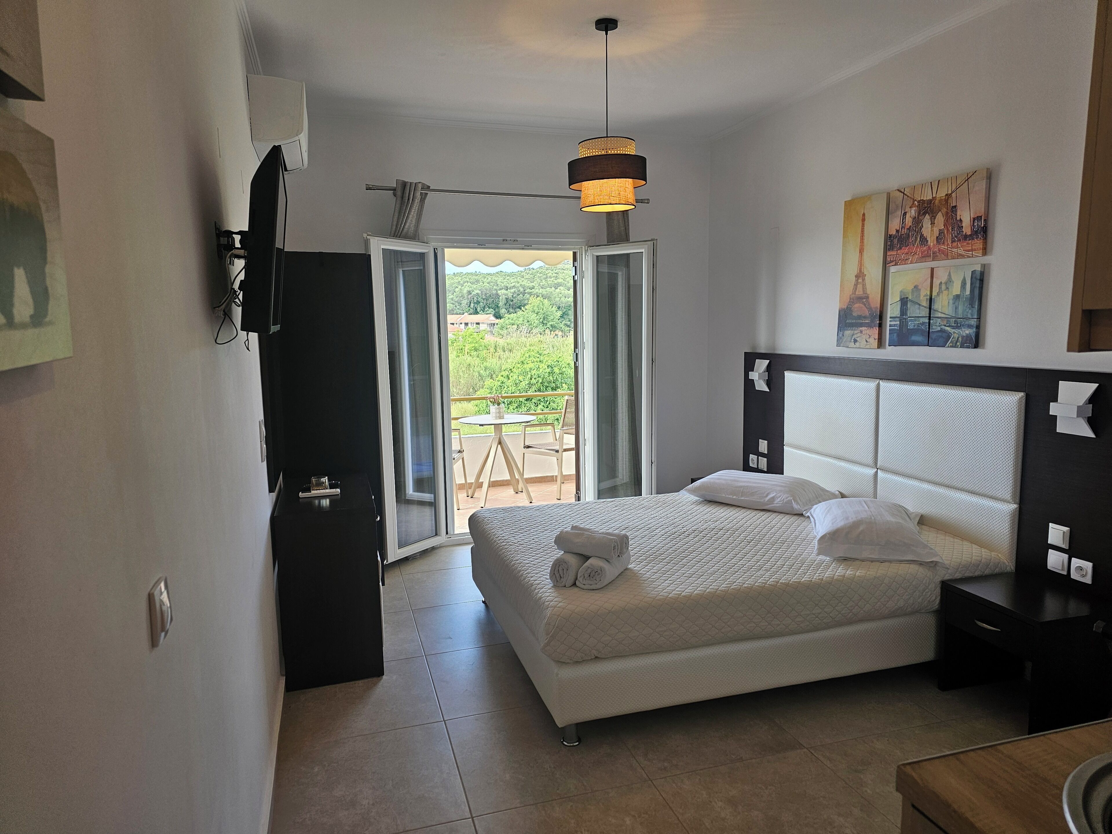 A bedroom with a bed, a TV, a desk, and a balcony with a table and chairs.