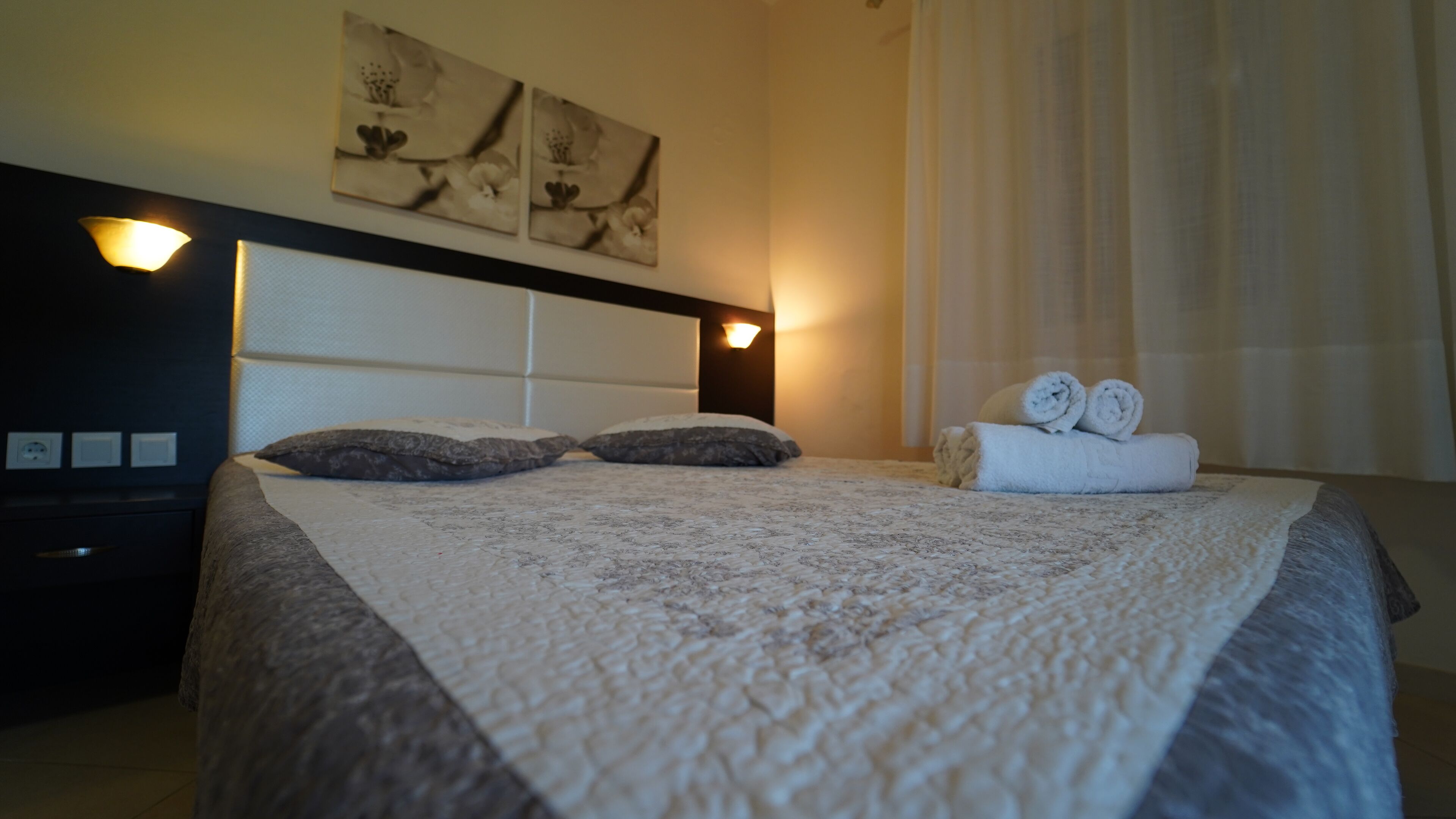 Una cama bien hecha con una colcha estampada, dos almohadas y toallas enrolladas al lado.