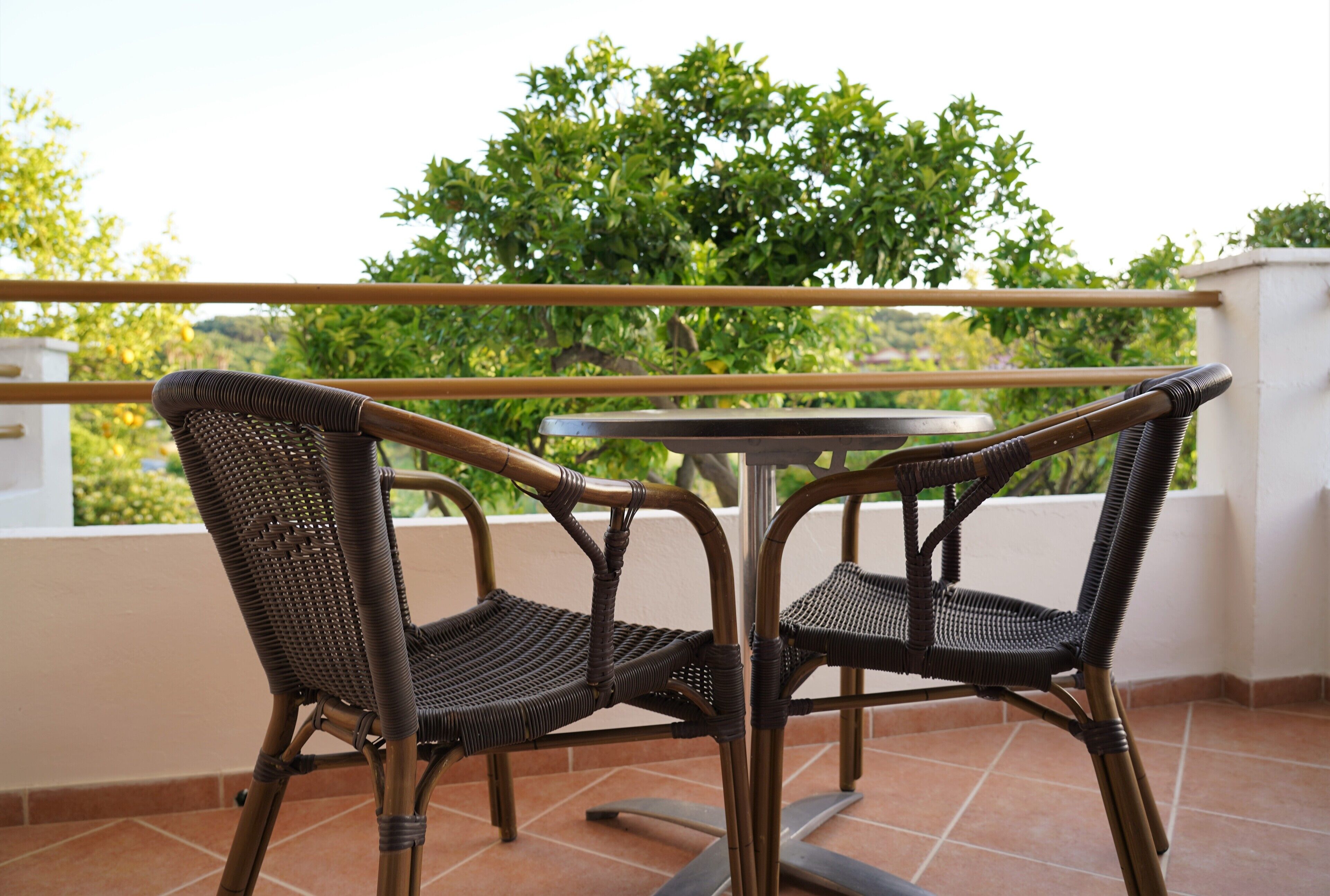 Une chaise et une table en osier sur un balcon donnant sur un paysage verdoyant.
