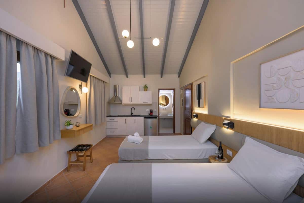 Quarto de hotel com duas camas, uma pequena cozinha, um espelho e uma televisão.