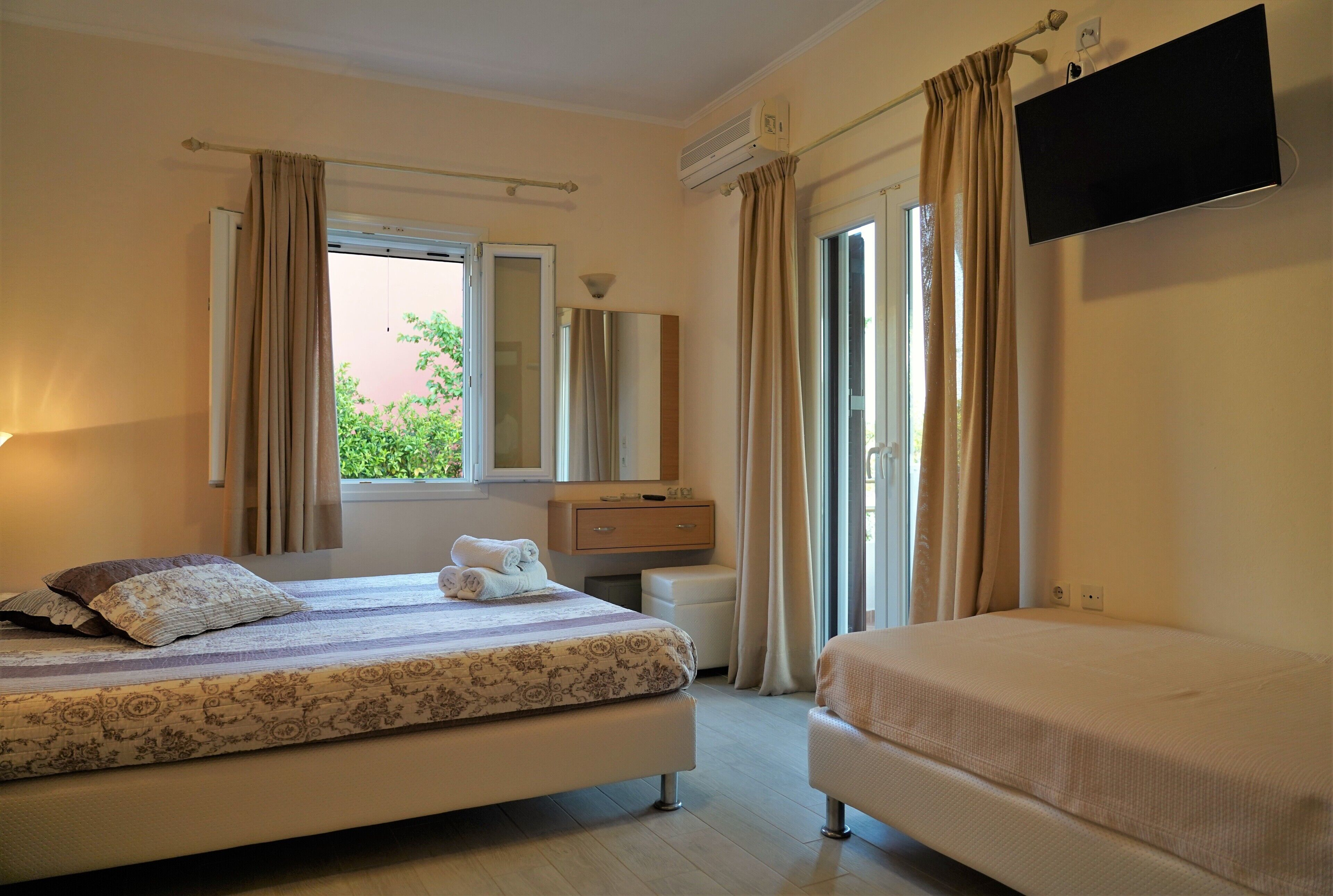 A hotel room with a bed, a bedside table, a mirror, a TV, and a window with curtains.