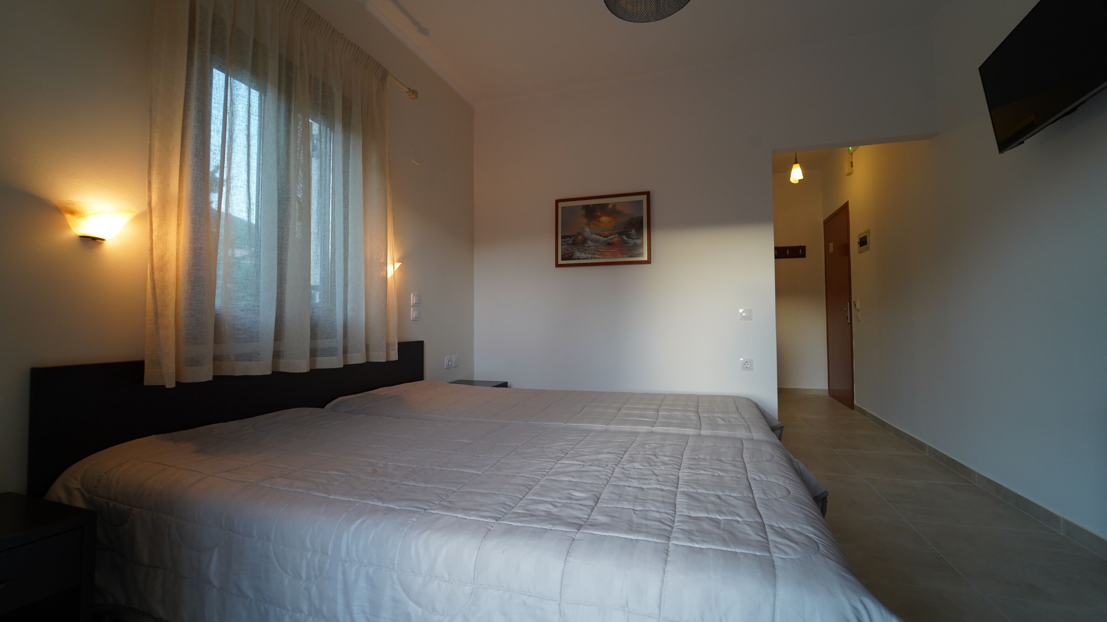 A bedroom with a large bed, a painting on the wall, and a hallway leading to another room.