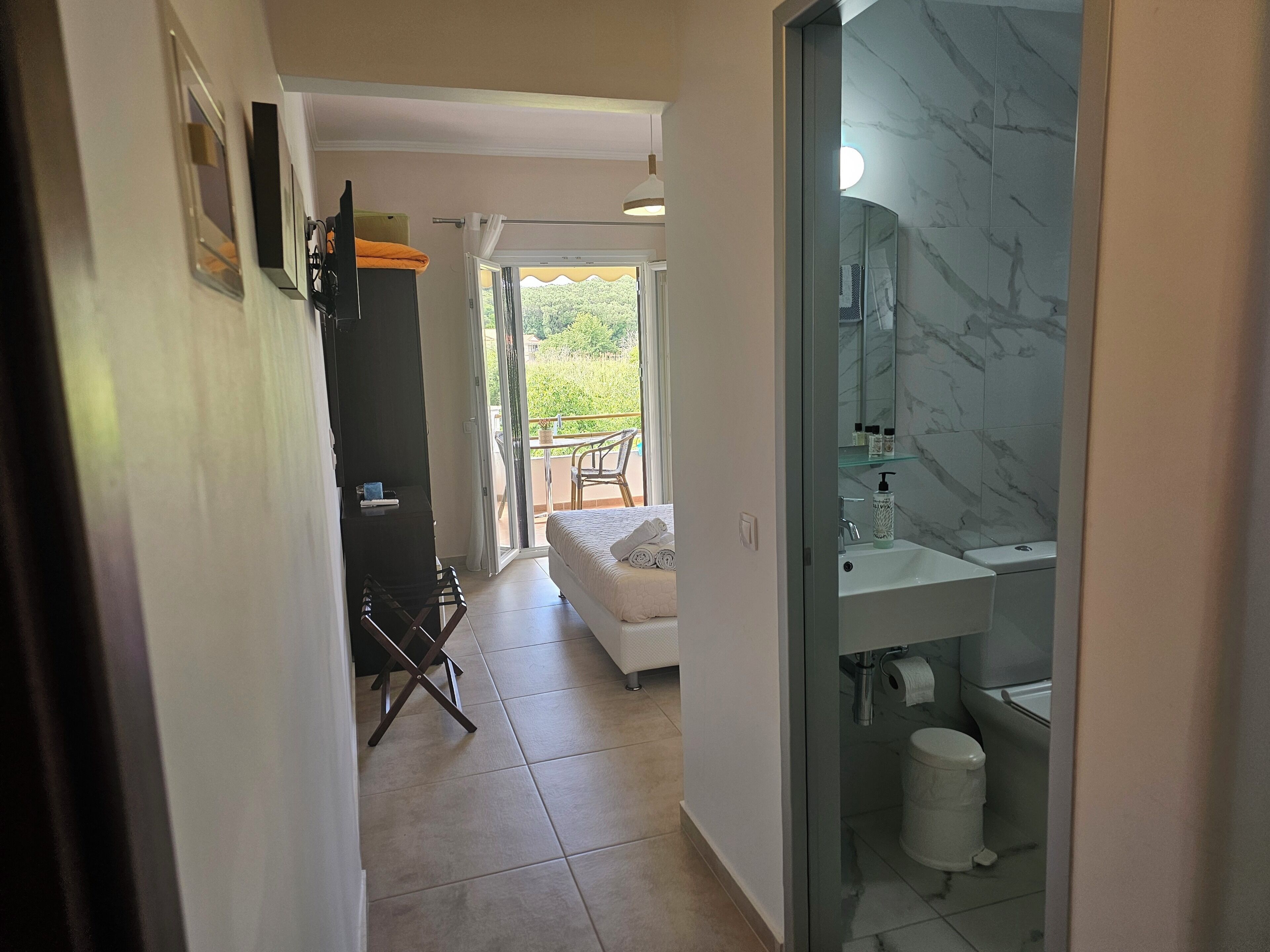 Habitación de hotel con balcón, una cama, baño con lavamanos de mármol y una silla cerca de la ventana.