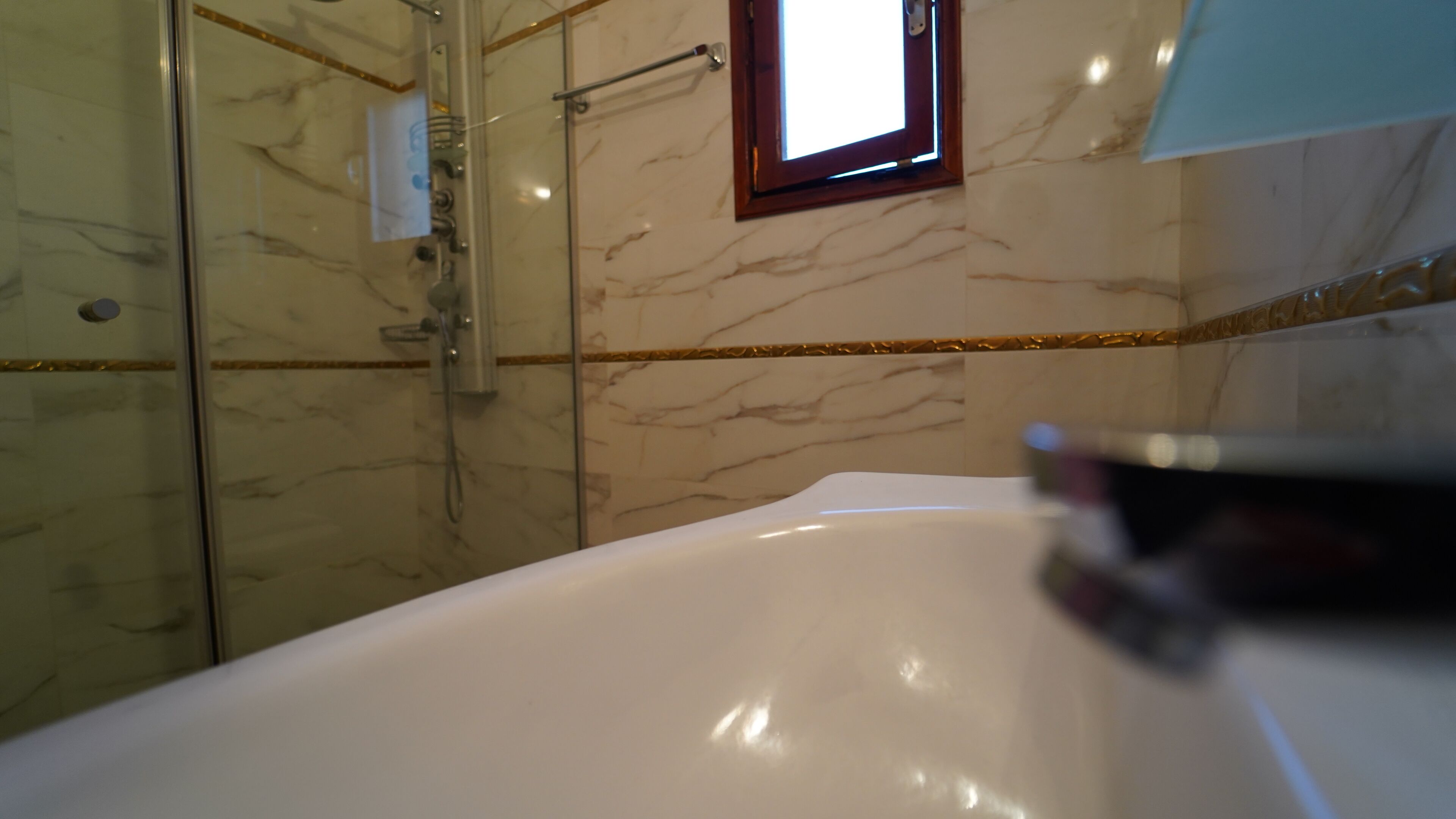 Une salle de bain avec une baignoire, une cabine de douche en verre et un mur de marbre agrémenté d'une bordure dorée.