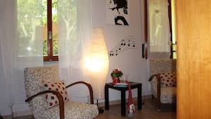 A room with two floral-patterned chairs, a table with a lamp, and a wall with a silhouette and musical notes. - Sa Babbaiola B&B (Cagliari)