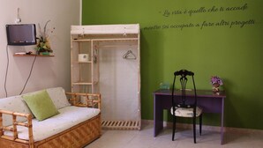 A room with a green wall, a wooden sofa, a small table, a chair, a TV, and a wardrobe. - Sa Babbaiola B&B (Cagliari)