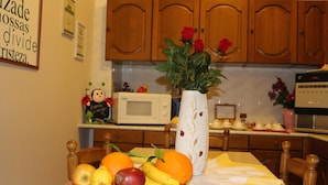 A kitchen with wooden cabinets, a microwave, and a table with fruits and a vase with flowers. - Sa Babbaiola B&B (Cagliari)