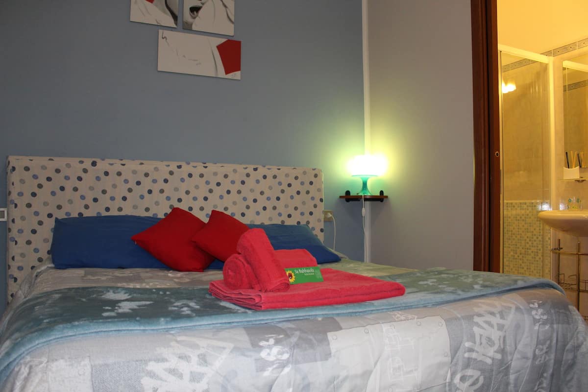 A neatly made bed with a polka dot headboard, red and blue pillows, and a folded red towel with a tag.