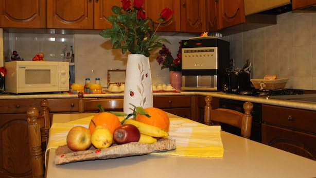 A kitchen with wooden cabinets, a microwave, a coffee maker, and a fruit and flower arrangement on the counter. - Sa Babbaiola B&B (Cagliari)