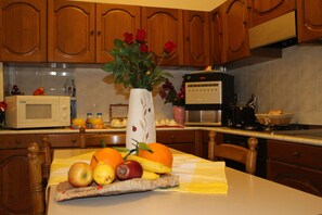 Una cocina con armarios de madera, microondas, cafetera y una decoración de frutas y flores en la encimera.