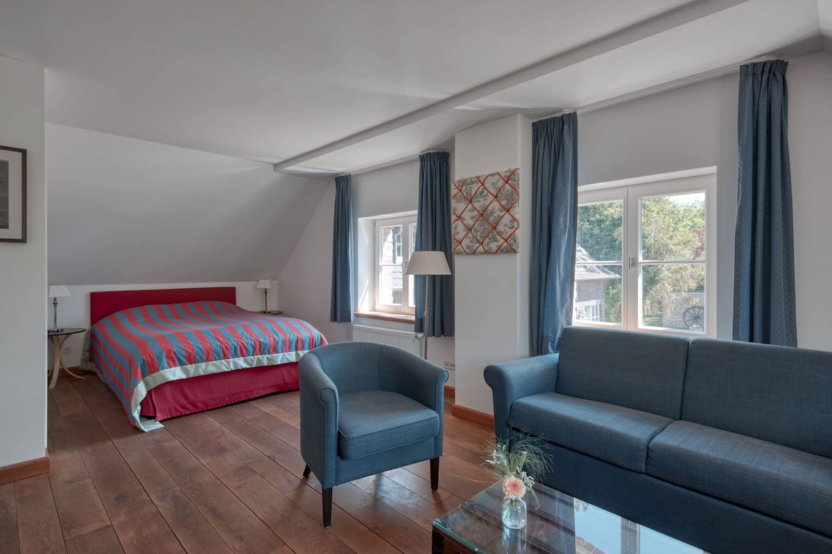 A room with a bed, two sofas, a lamp, and a window with curtains.