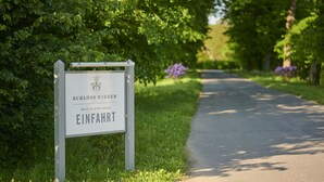 A sign with the text "SCHLOSS WISSEN EINFAHRT" in a garden setting.