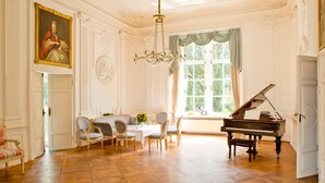 A grand room with a piano, elegant chairs, a dining table, and a large window with curtains.