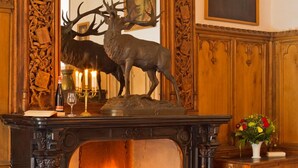 A fireplace with a deer sculpture, a framed portrait, and a vase of flowers.
